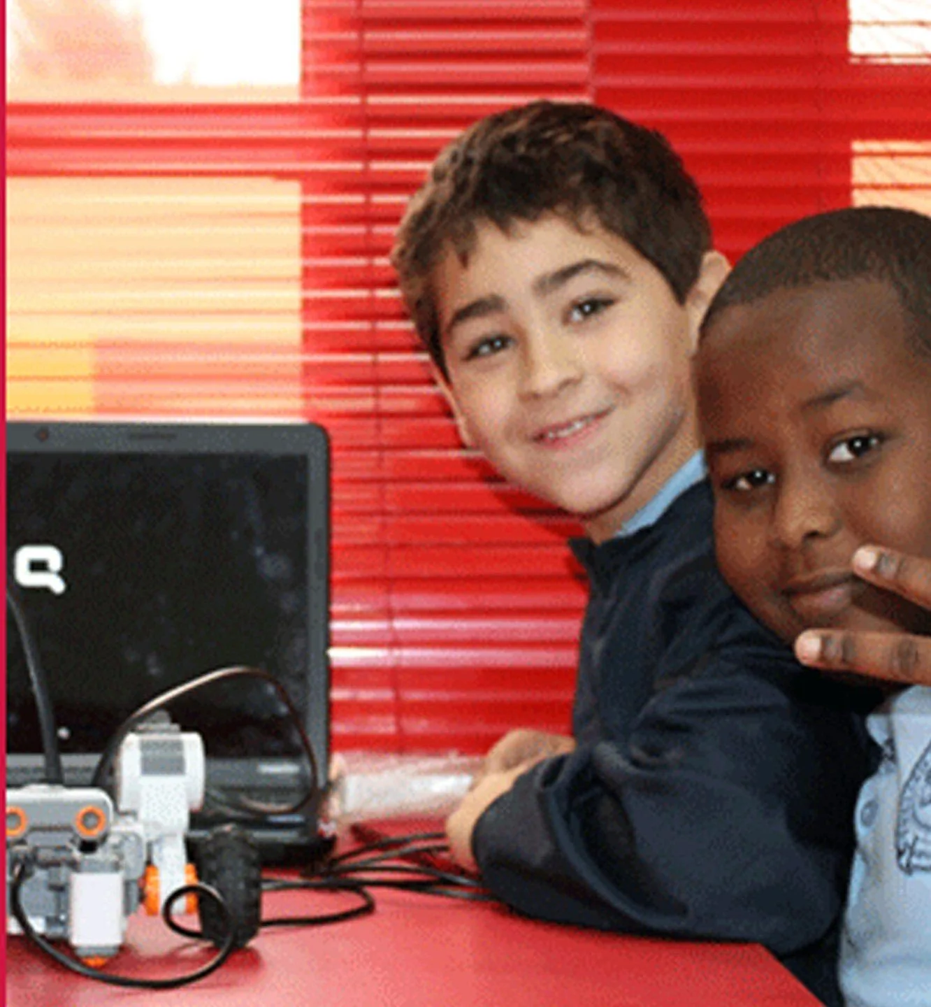 Two students working at a laptop beside a robot they have built
