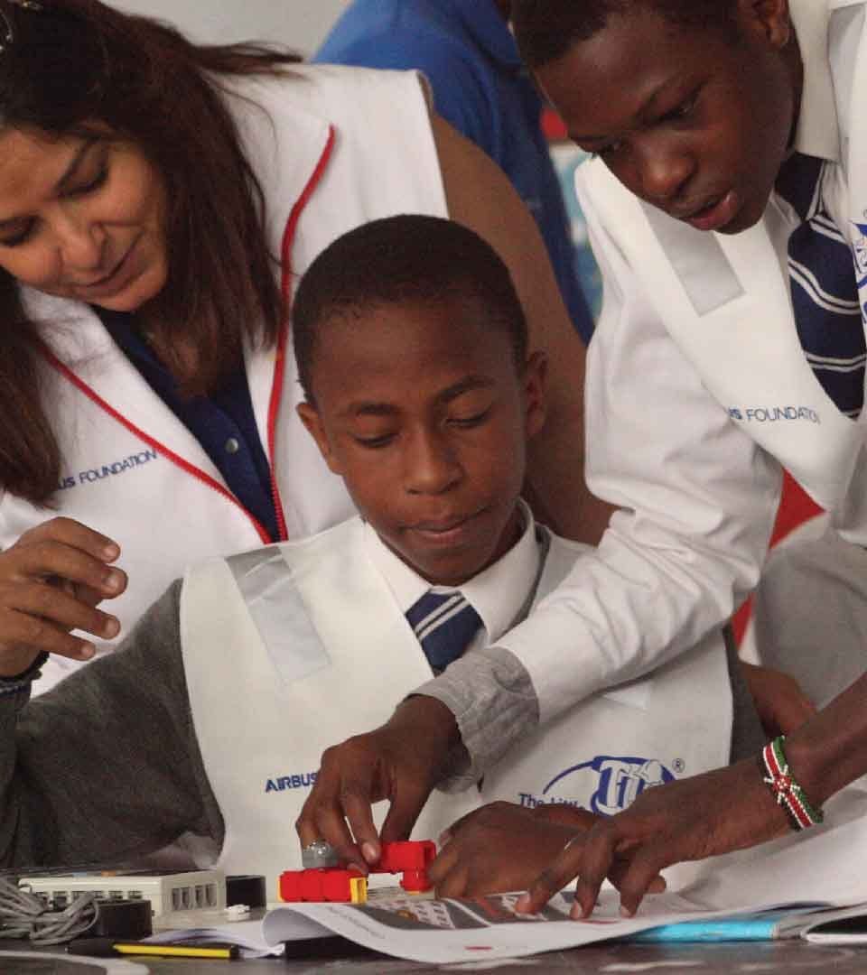 An instructor guiding students wearing Airbus Foundation and Little Engineer vests through a build