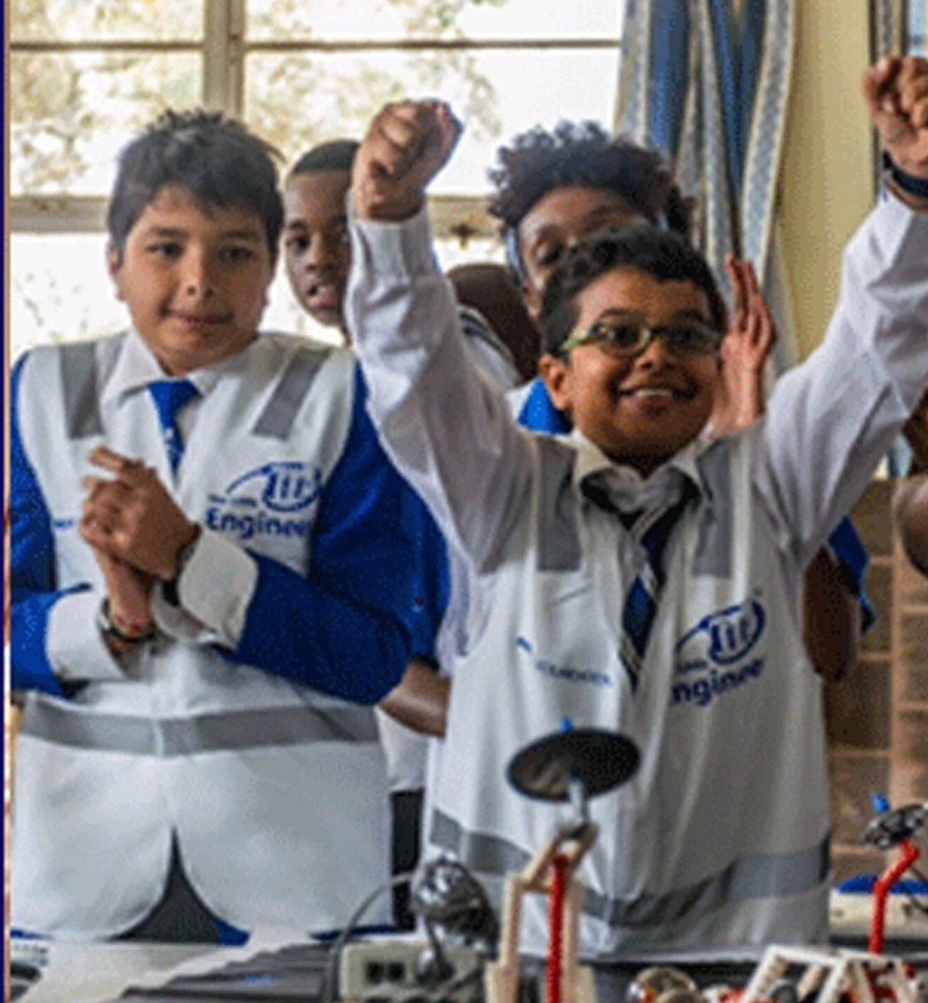 Students in Little Engineer lab coats celebrating a successful build in a robotics session