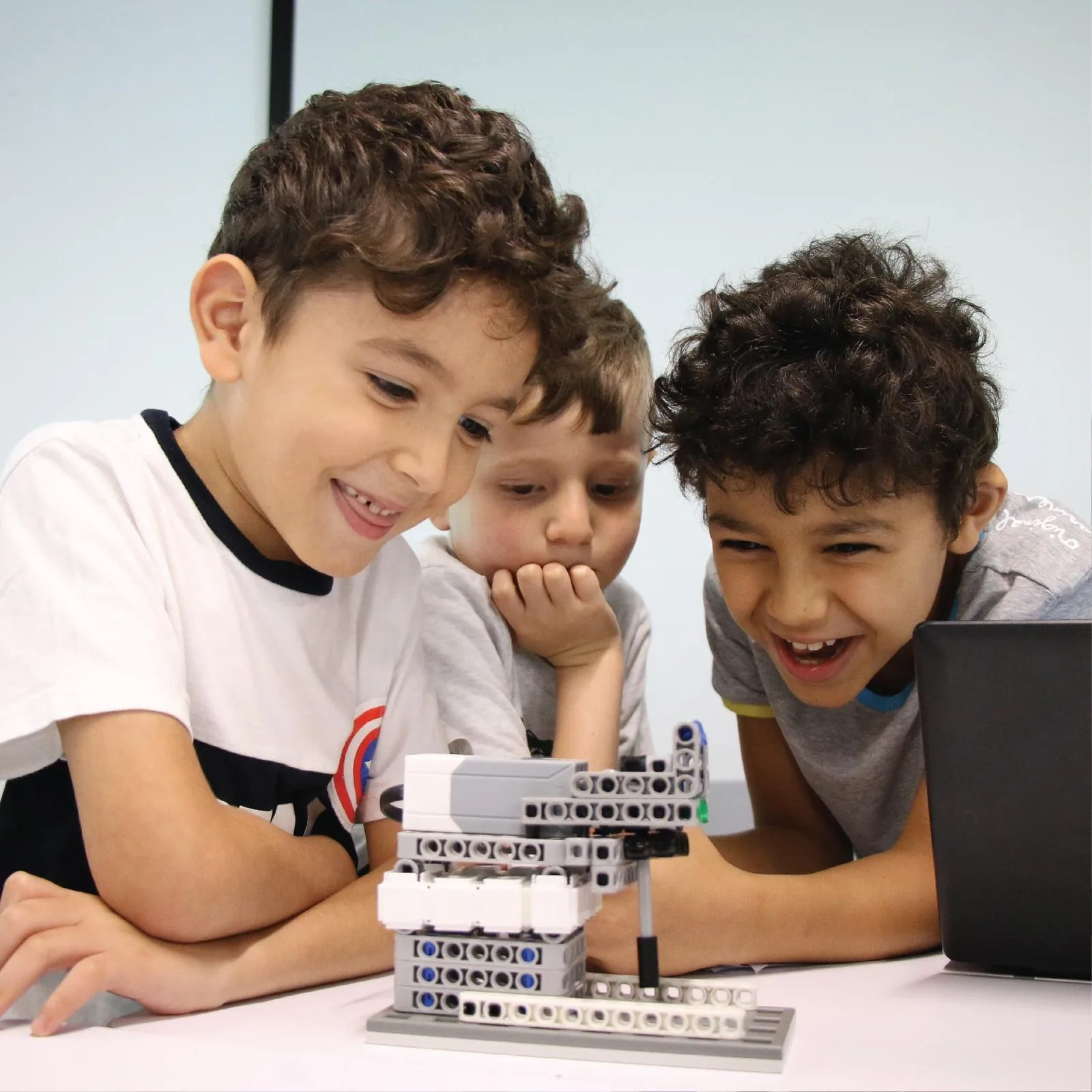 Three children laughing together while coding a model they have built
