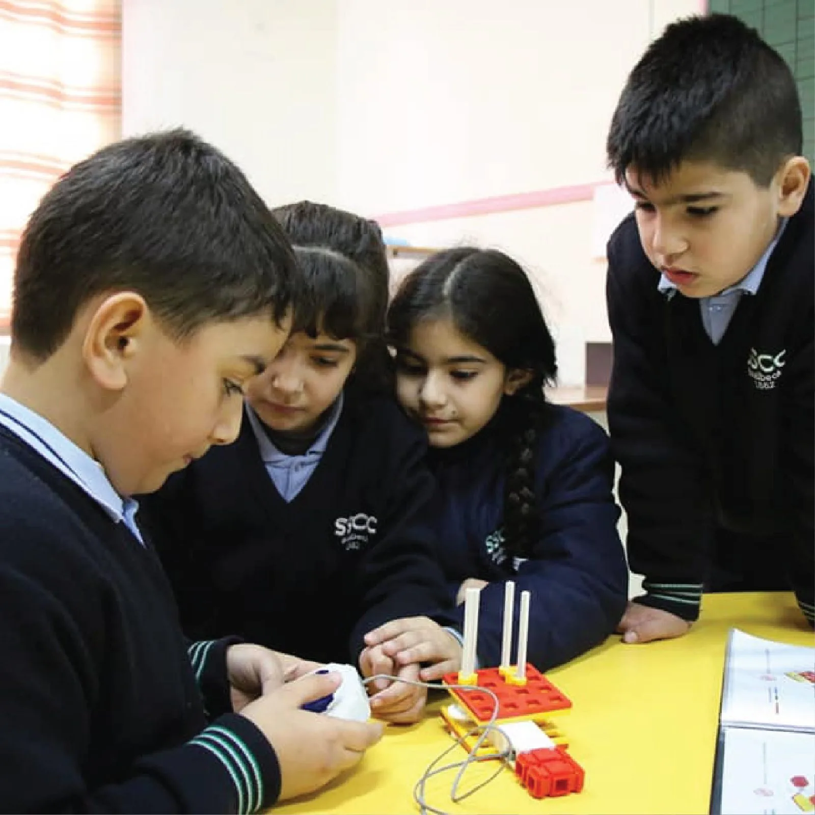School students in uniform working together on a robotics kit at a classroom table